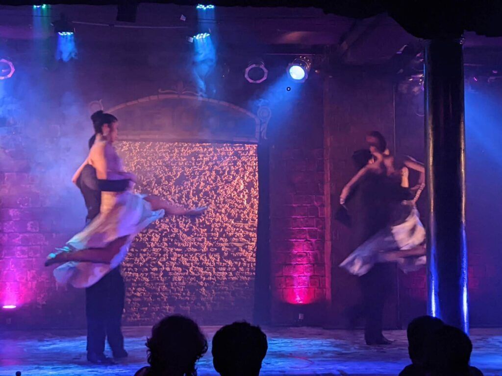 A couple performs a passionate tango dance on stage, with elegant costumes and dramatic lighting enhancing the atmosphere of a live show.