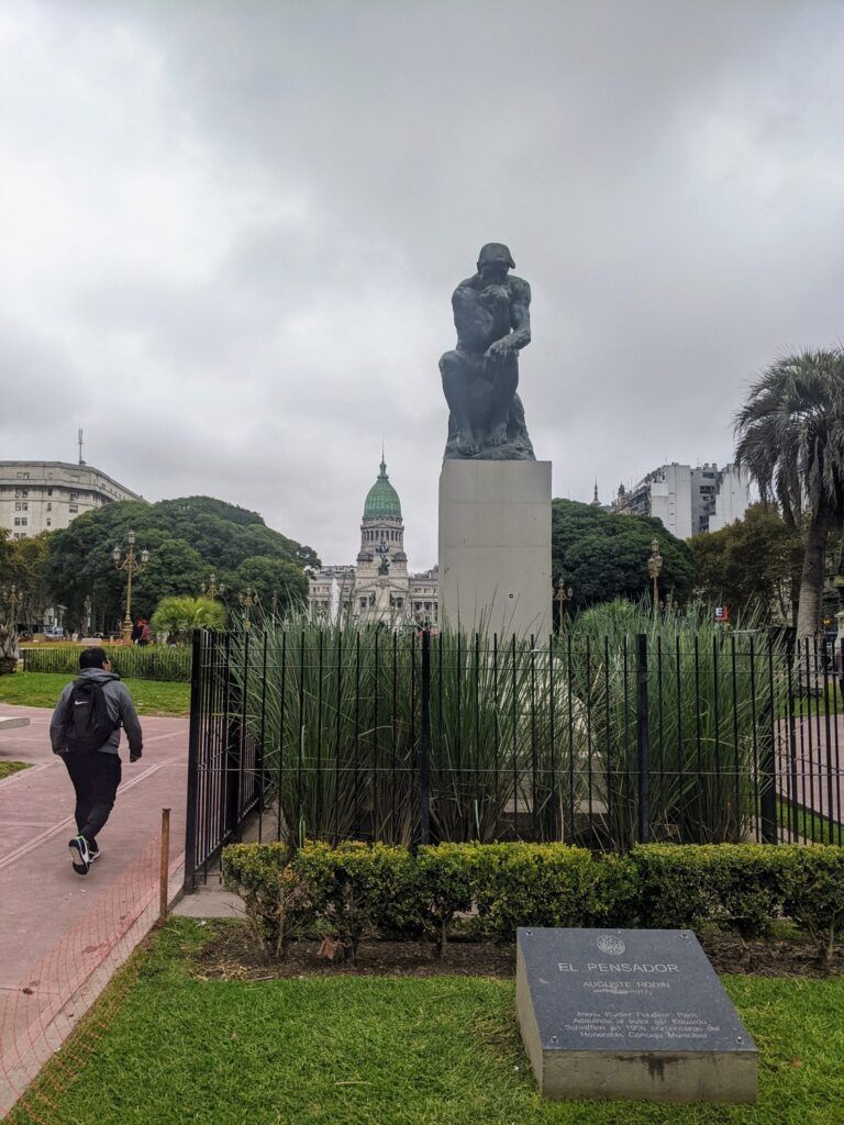 View of Palacio Barolo in Buenos Aires, a historic tower with intricate architectural details, accompanied by a statue of The Thinker, emphasizing the city's cultural richness.