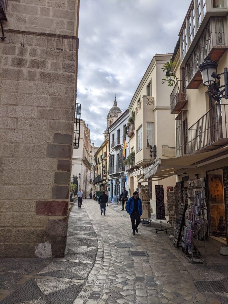A street scene in Málaga, Spain, with people walking around shops and cafés, discussing non-water activities and cultural experiences such as visiting museums.