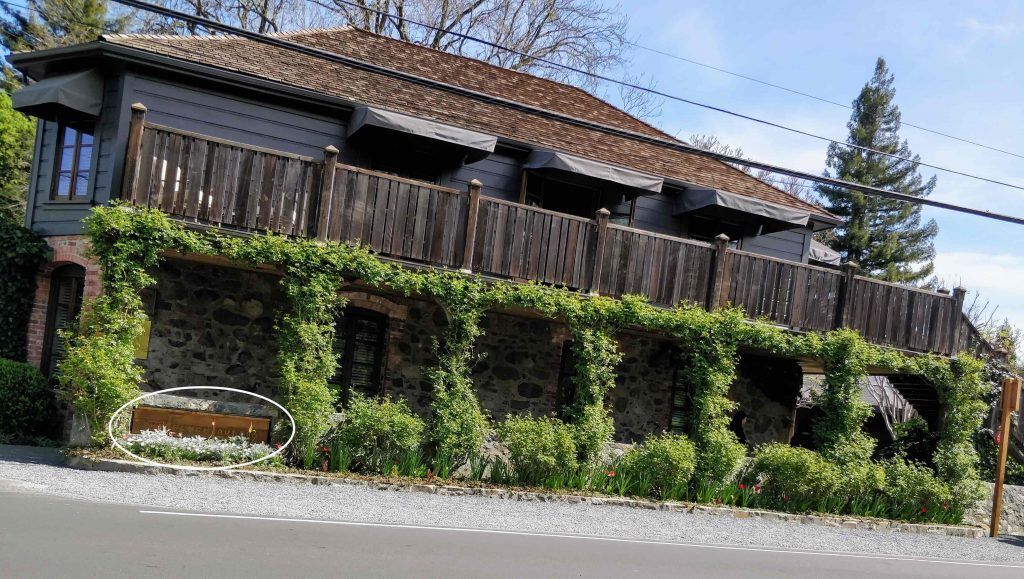 Front view of a simple, understated restaurant exterior, partially obscured by trees and landscaping, providing a low-key, easily overlooked entrance to French Laundry