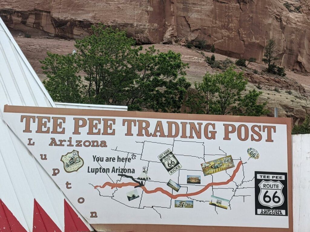 A large teepee structure stands prominently beside the road, serving as the Tee Pee Trading Post, surrounded by a few small structures and vehicles.