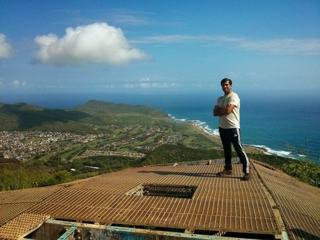 A scenic view of a small island, known as Chinaman's Hat, with lush greenery and surrounded by ocean waters, set against a clear sky.