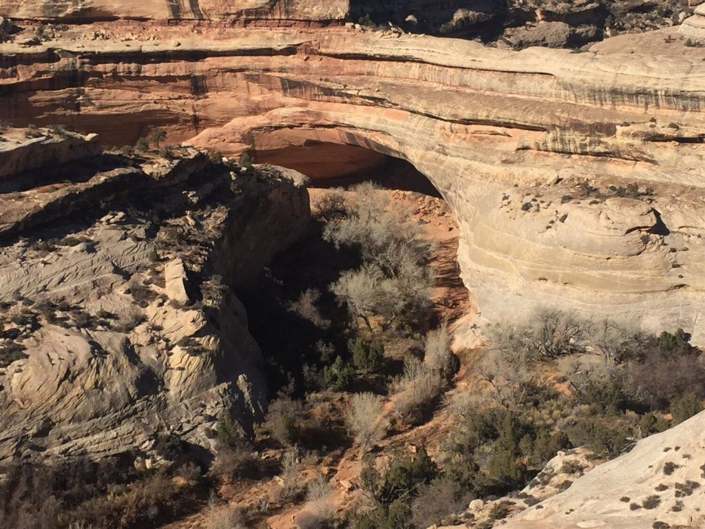 A natural rock bridge spans across a canyon landscape. It's a popular but time-consuming hiking destination, best viewed after completing a trail.