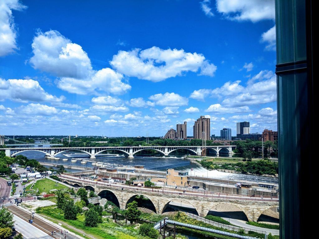 A scenic view of a waterfall surrounded by lush greenery and rocky formations, with information about flour production in the world and a mention of the Stone Arch Bridge's view.