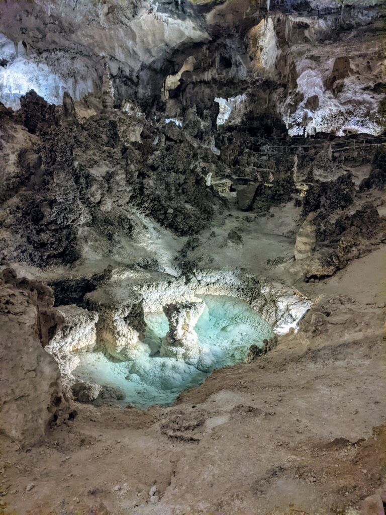 A rocky, dimly lit cavern interior with large stalactites and stalagmites, showcasing a natural, underground landscape.