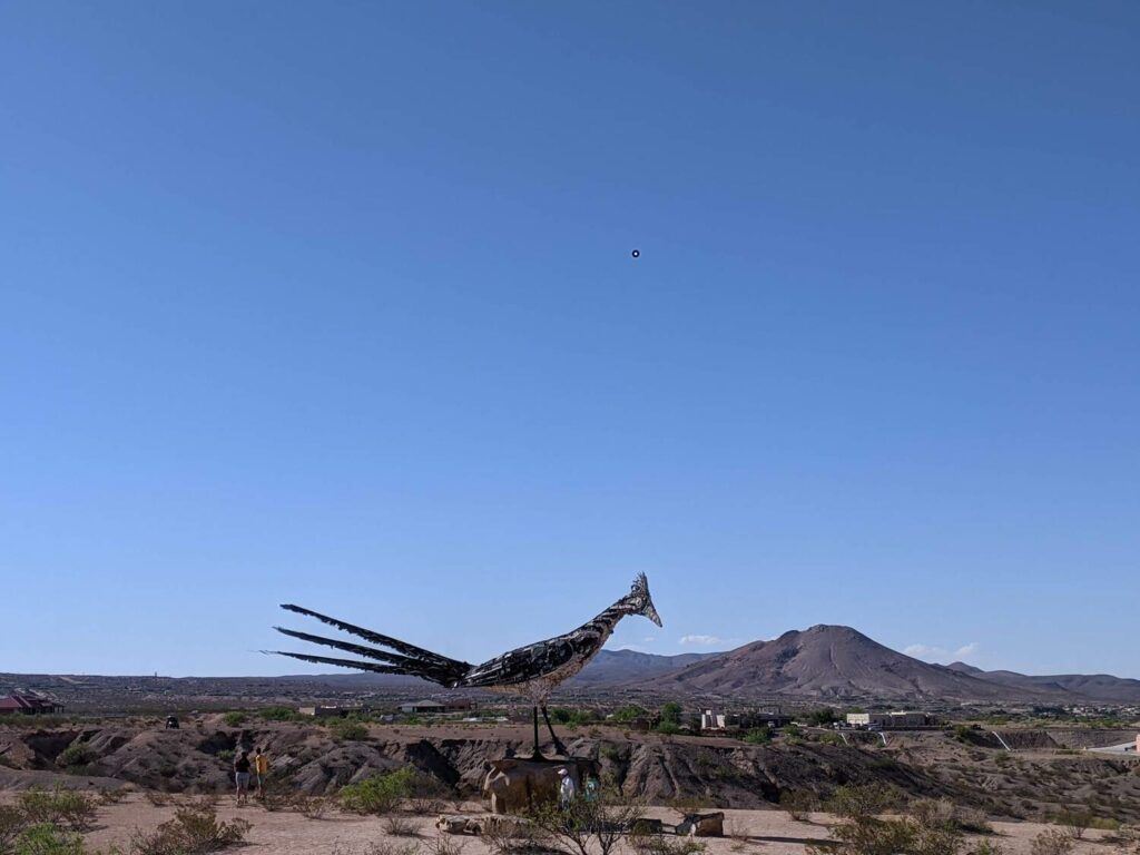 A large sculpture of a roadrunner created from recycled materials, located near Las Cruces, New Mexico, stands prominently against a desert landscape backdrop.