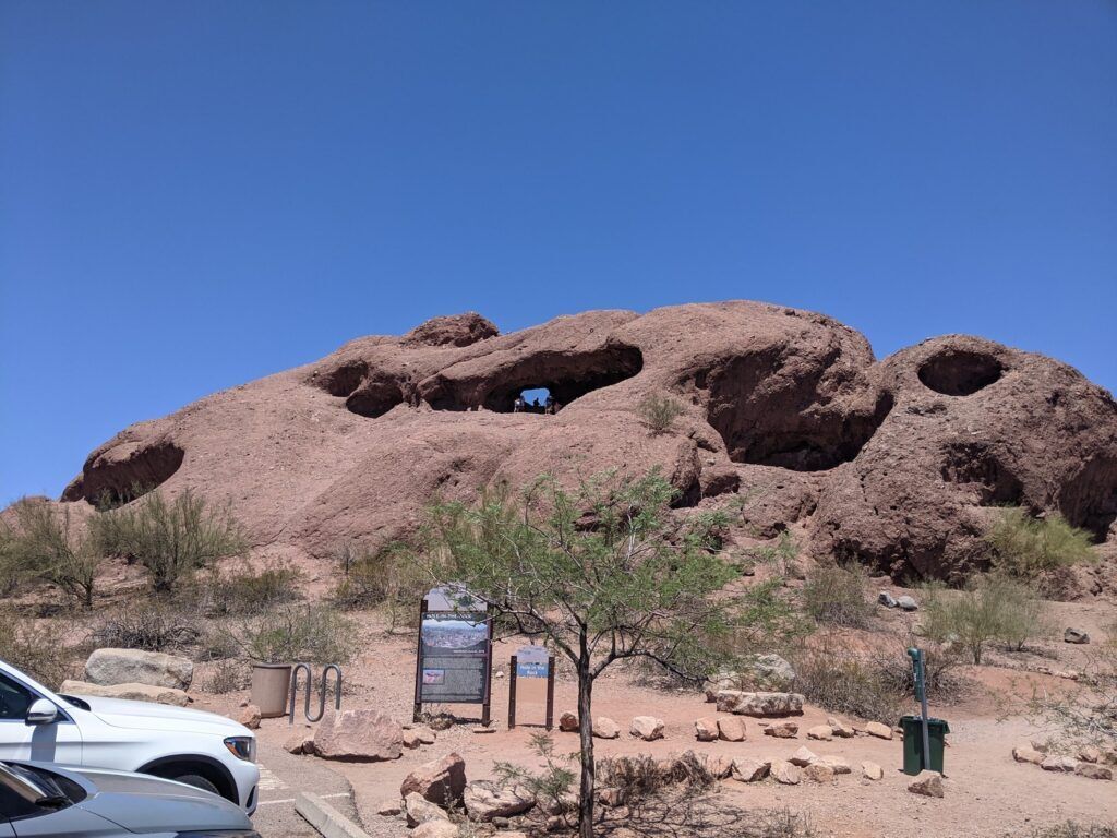 A large rock formation with a distinctive hole near the top, set in a desert landscape under a clear blue sky.